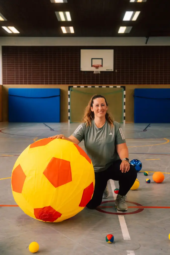 Kinder in Bewegung von Lisa Haas - Foto zeigt Lisa Haas in der Turnhall mit vielen Bällen und einem sehr großen Ball
